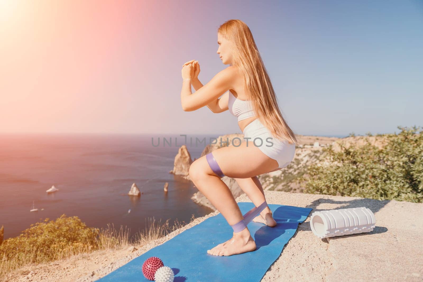 Woman sea pilates. Sporty happy middle aged woman practicing fitness on yoga mat using rubber tape, massage balls, and rollers near sea, smiling active female outside, enjoying healthy lifestyle by panophotograph