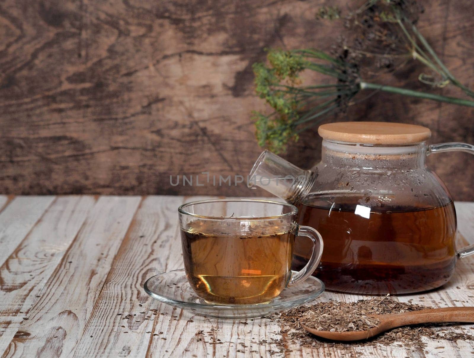 Medicinal tea using dried dill seeds in a cup and teapot on a natural wooden table.