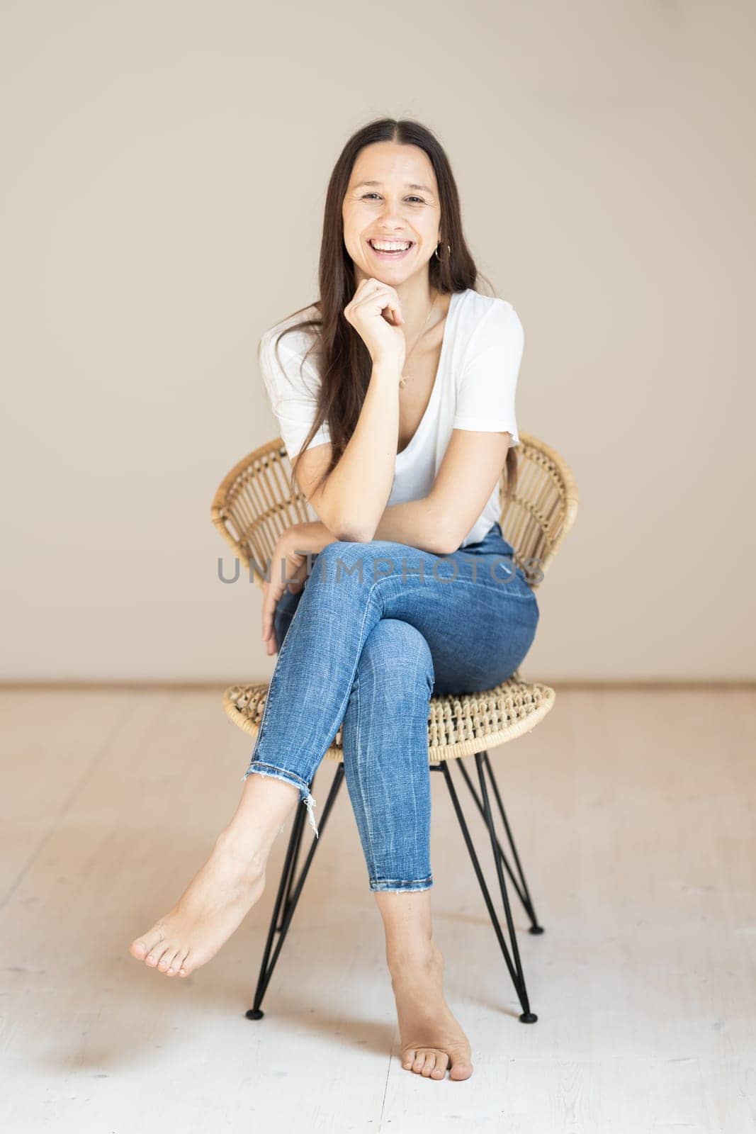 Portrait of confident beautiful woman with long brown hair, wearing casual clothes, sitting on chair in tight jeans and white t-shirt, studio background by kasto