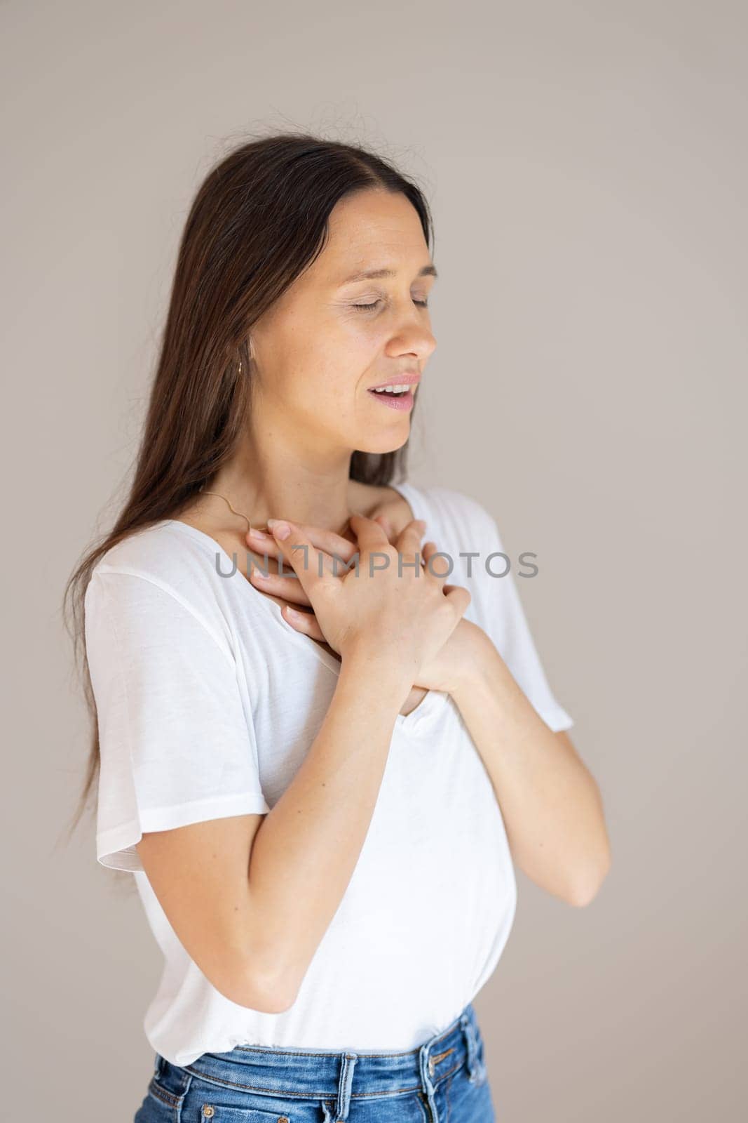 Portrait of confident beautiful woman with long brown hair, wearing casual clothes, standing in relaxed pose with hands on chest, breathing deeply, doing breathing exercise by kasto