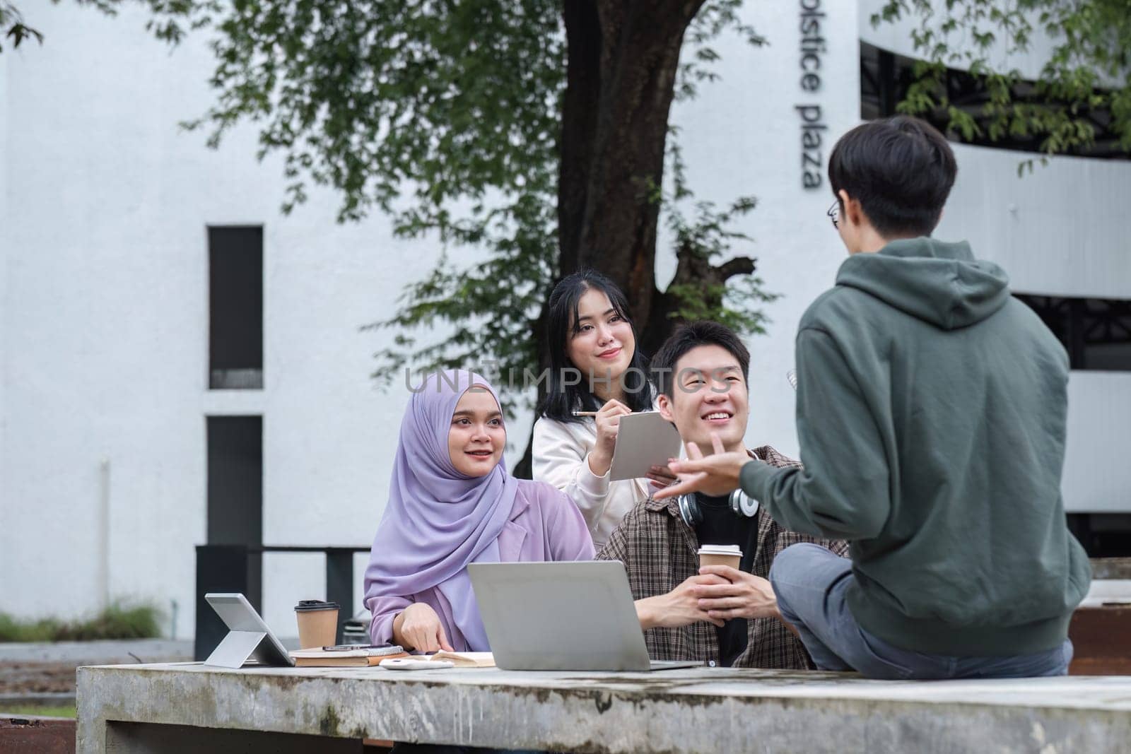 A multiracial group of students at the college, including Muslim and Asian students, sat on benches in a campus break area. Read books or study for exams together. by wichayada