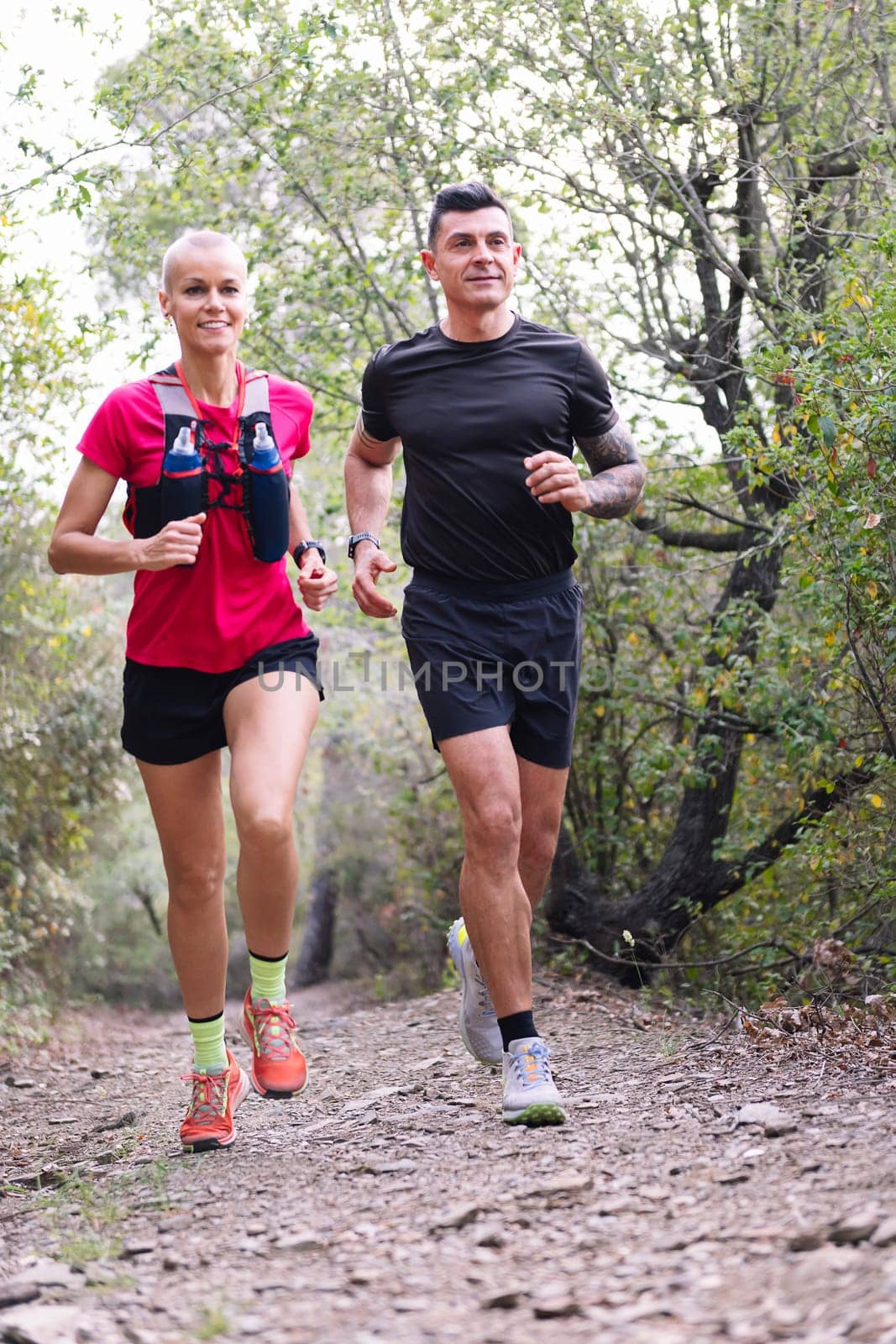 vertical photo of a couple practicing trail running in the forest, concept of sport in nature and healthy lifestyle, copy space for text