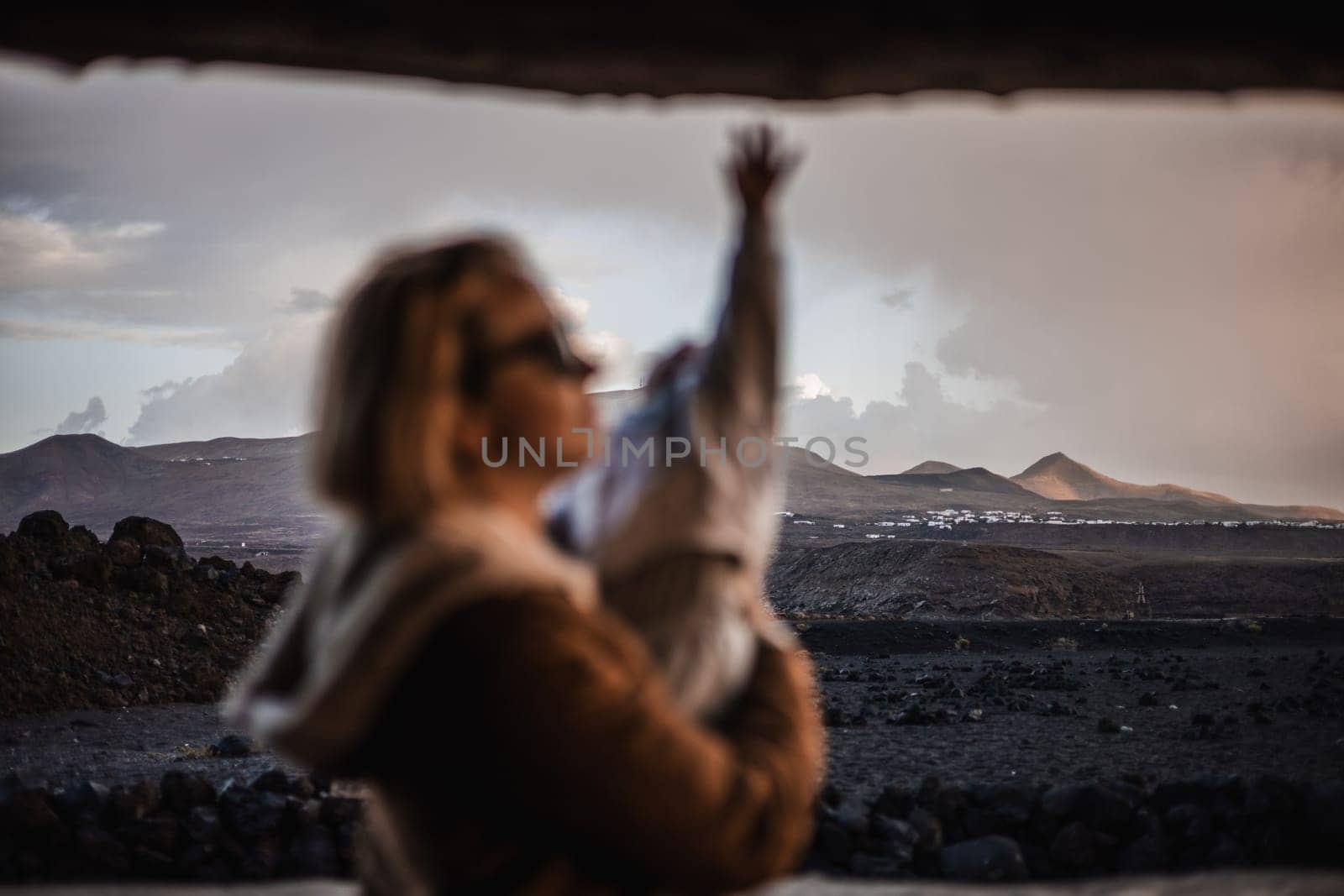 Mother enjoying winter vacations playing with his infant baby boy son on black sandy volcanic beach of Janubio on Lanzarote island, Spain on windy overcast day. Family travel vacations concept