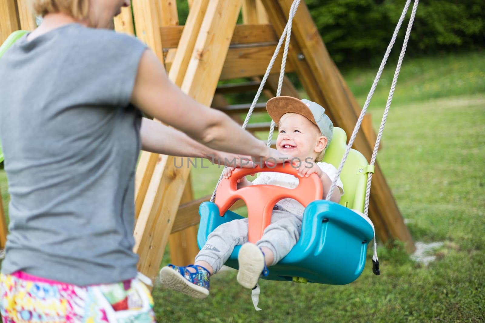 Mother pushing her infant baby boy child on a swing on playground outdoors. by kasto