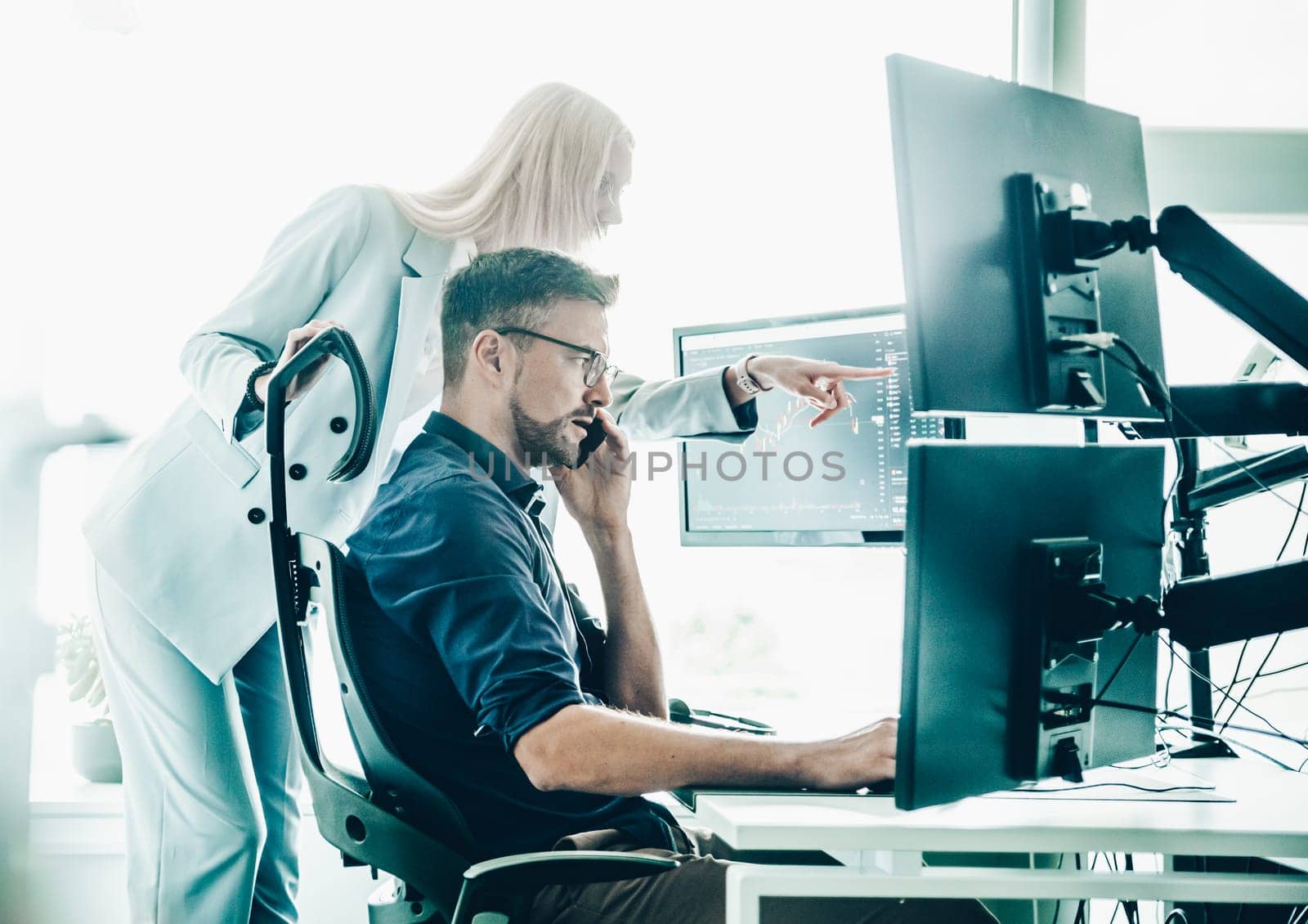 Stock broker business team trading online watching charts and data analyses on multiple computer screens in modern corporate work station office.