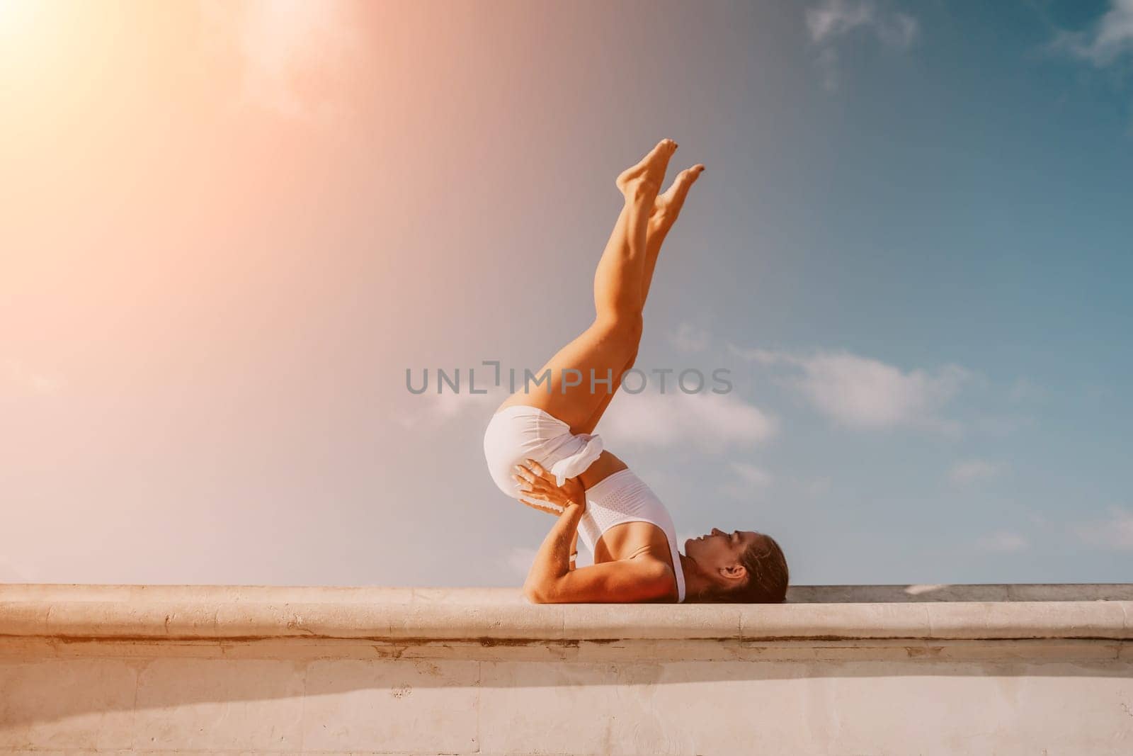 Fitness woman sea. A happy middle aged woman in white sportswear exercises morning outdoors in a park with a beach view. Female fitness pilates yoga routine concept. Healthy lifestyle. by panophotograph