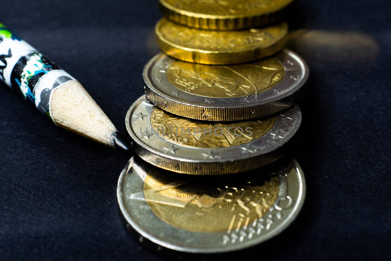 Money concept. Pencil with coins euro, close up, dark black background