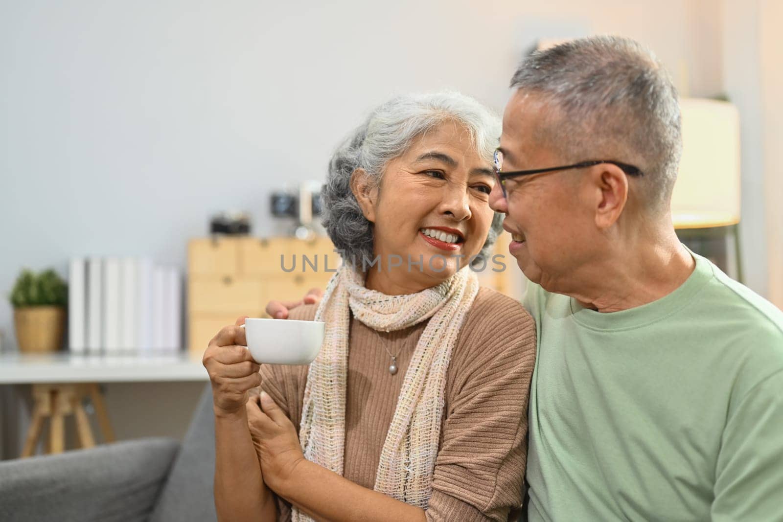Image of happy elderly couple drinking coffee chatting spending time together at home.