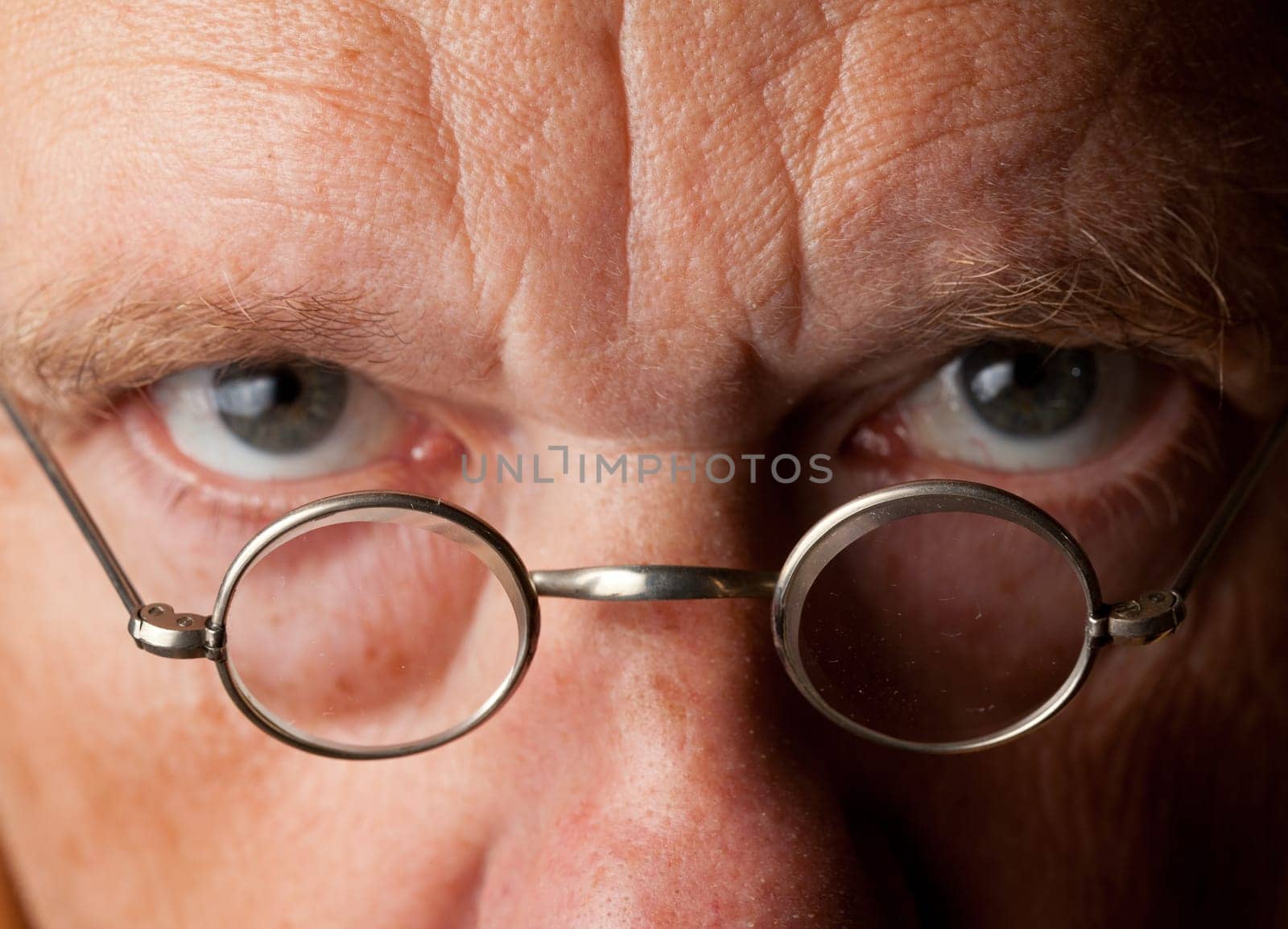 Portrait of a senior male with the focus on magnifying glasses and the eyes are blurred to suggest poor vision