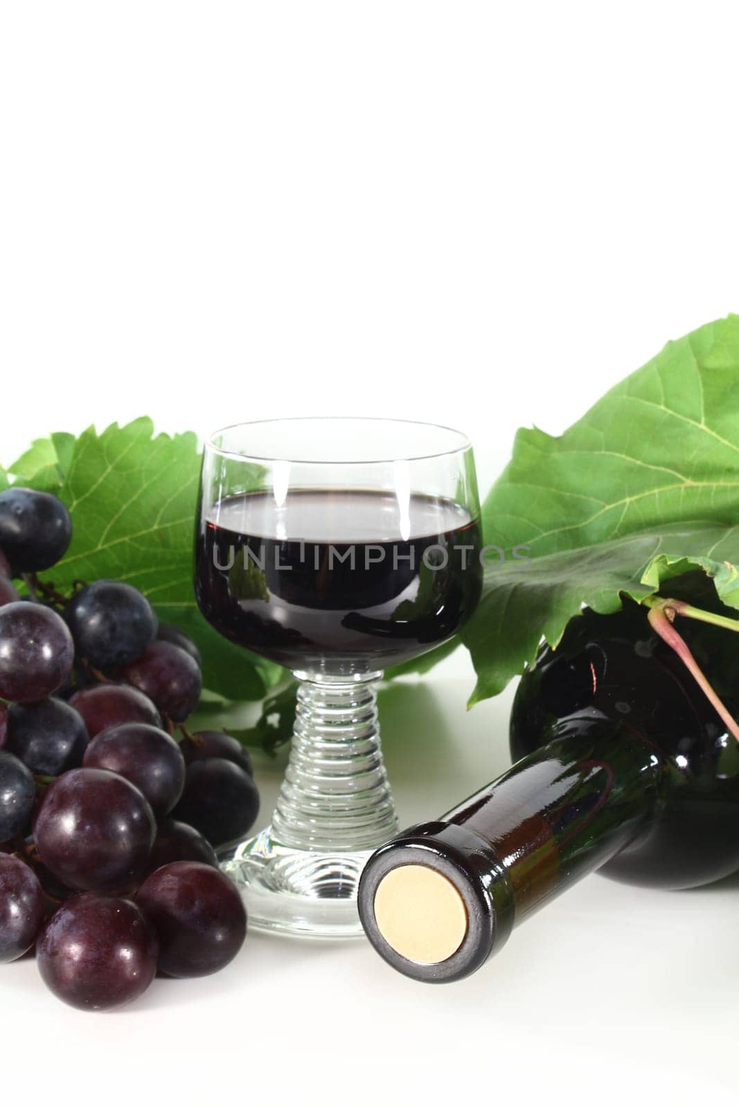 a bottle of red wine and fresh grapes against a white background