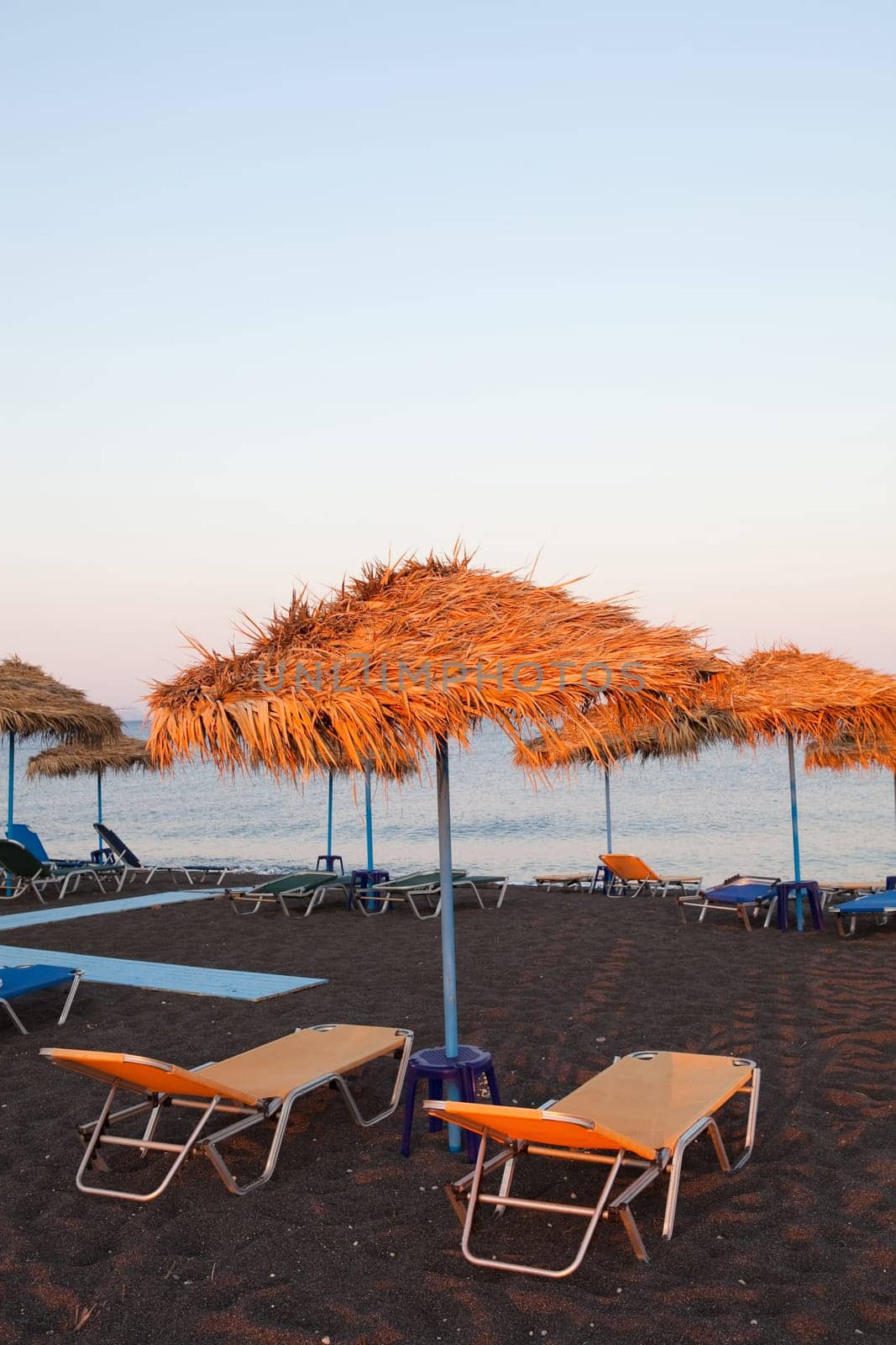 Beach umbrellas and sunbeds in evening sun in Perissa beach, Santorini, Greece