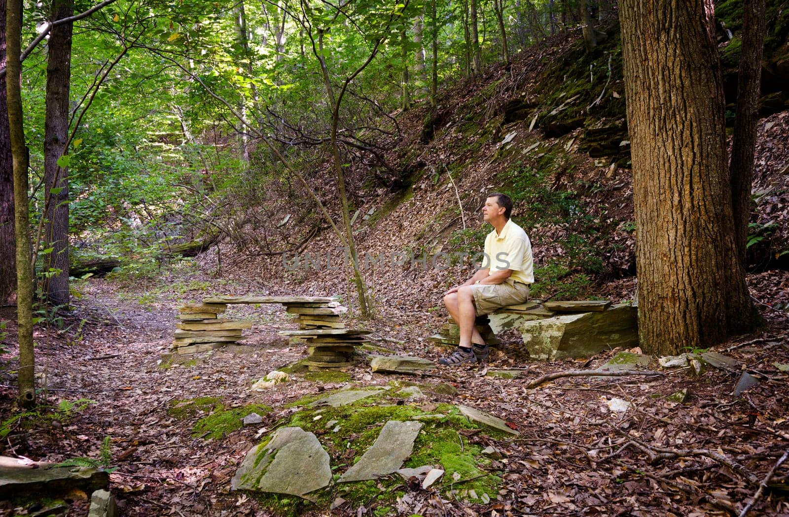 Retired hiker rests on stone benches in a clearing in a forest on a hike