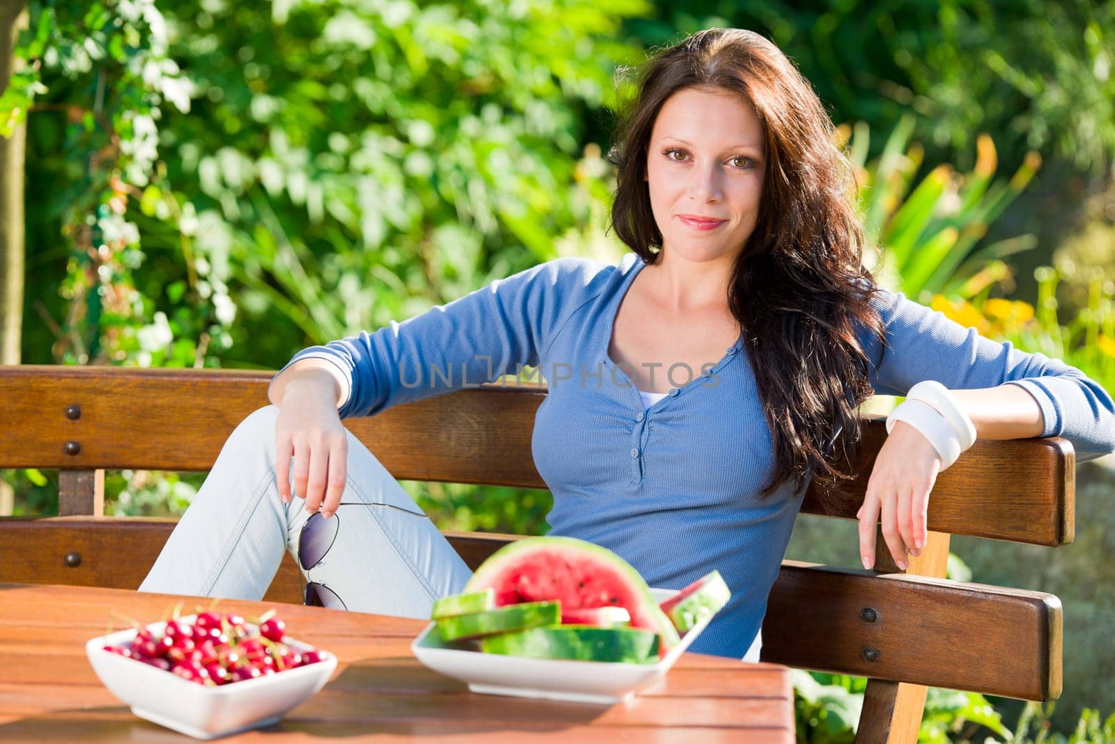 Beautiful young woman fresh summer fruit sitting on garden terrace