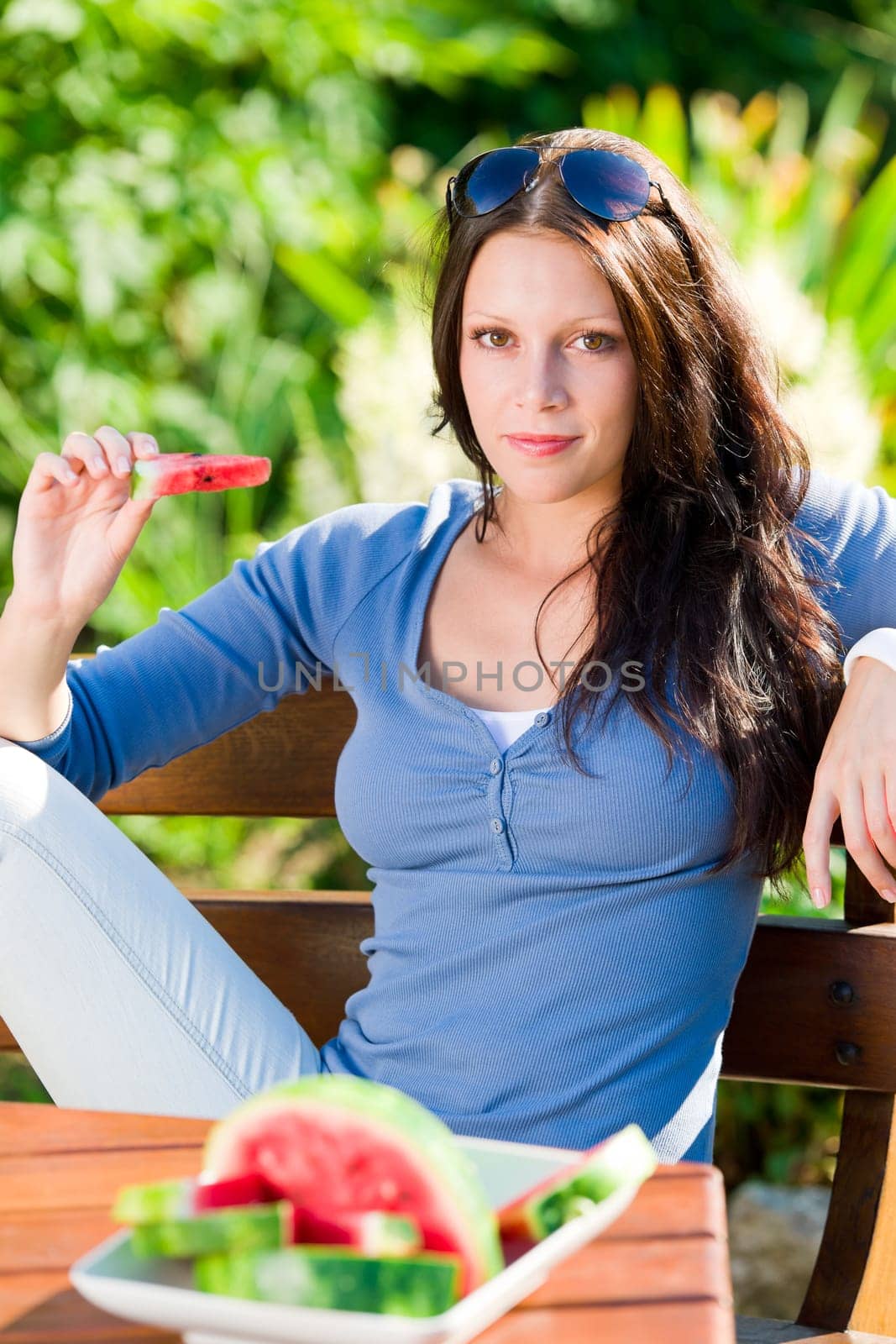 Beautiful young woman eating fresh melon sunny day garden bench