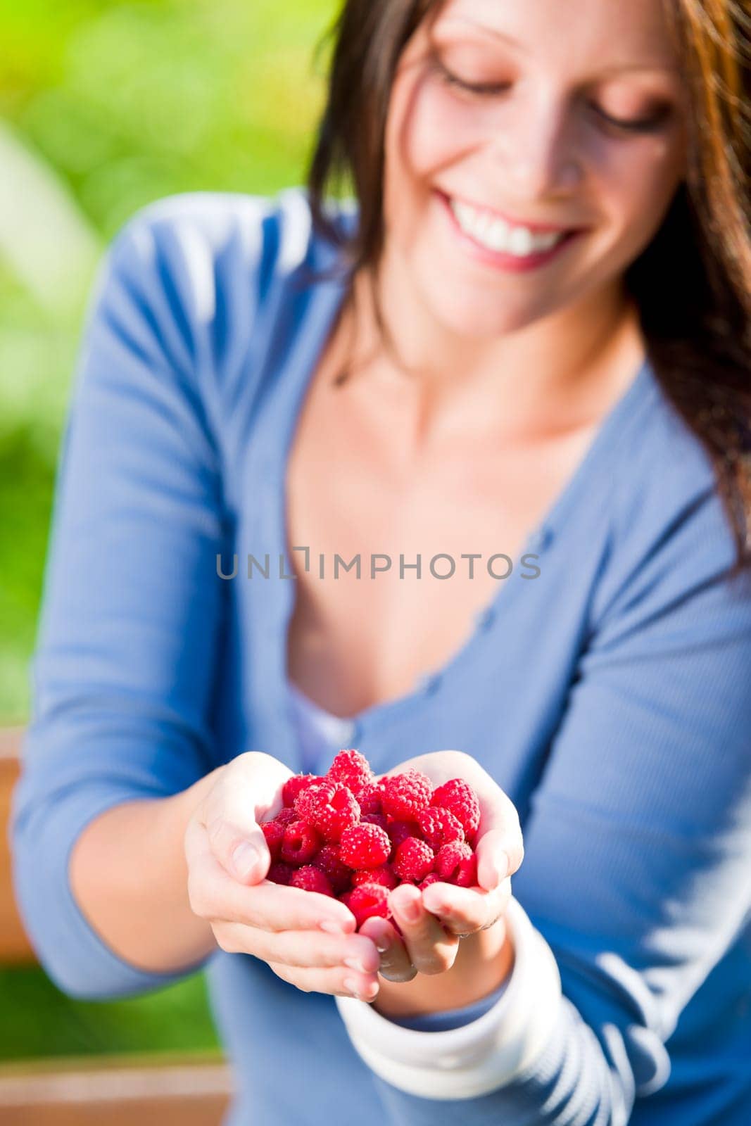 Happy young woman hold in hands fresh raspberries sunny day
