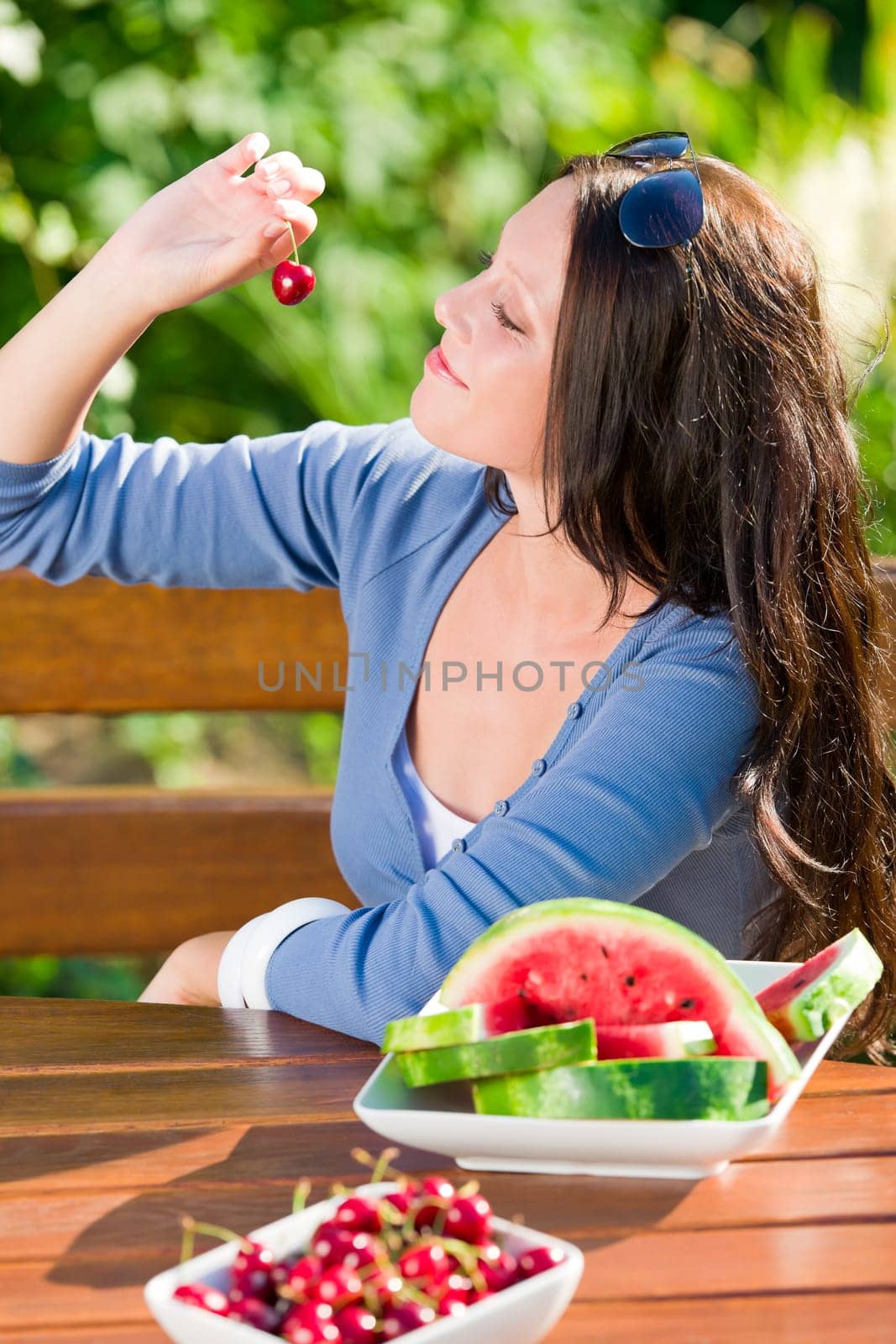 Beautiful young woman fresh summer melon cherries sitting garden terrace