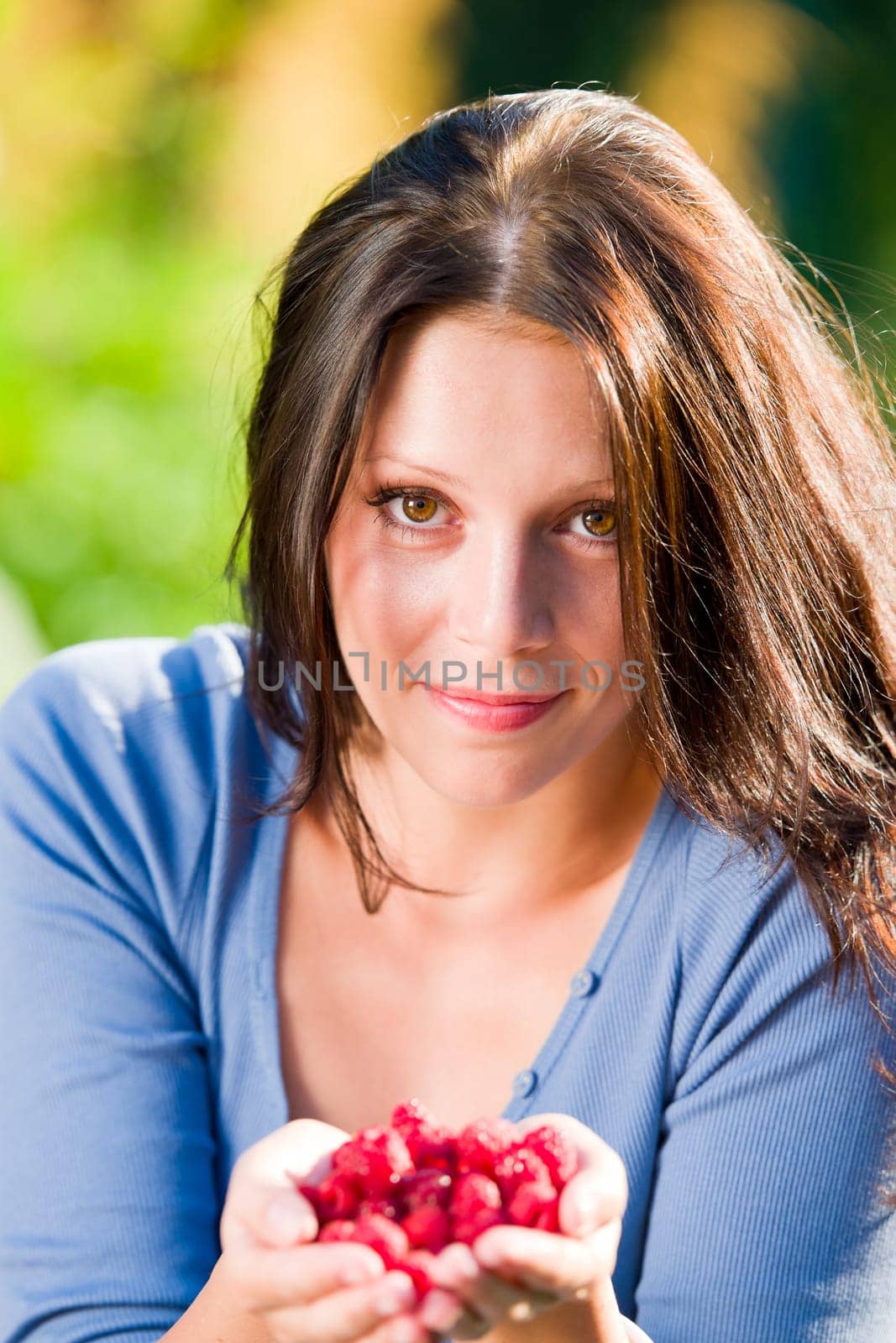 Happy young woman hold in hands fresh raspberries sunny day