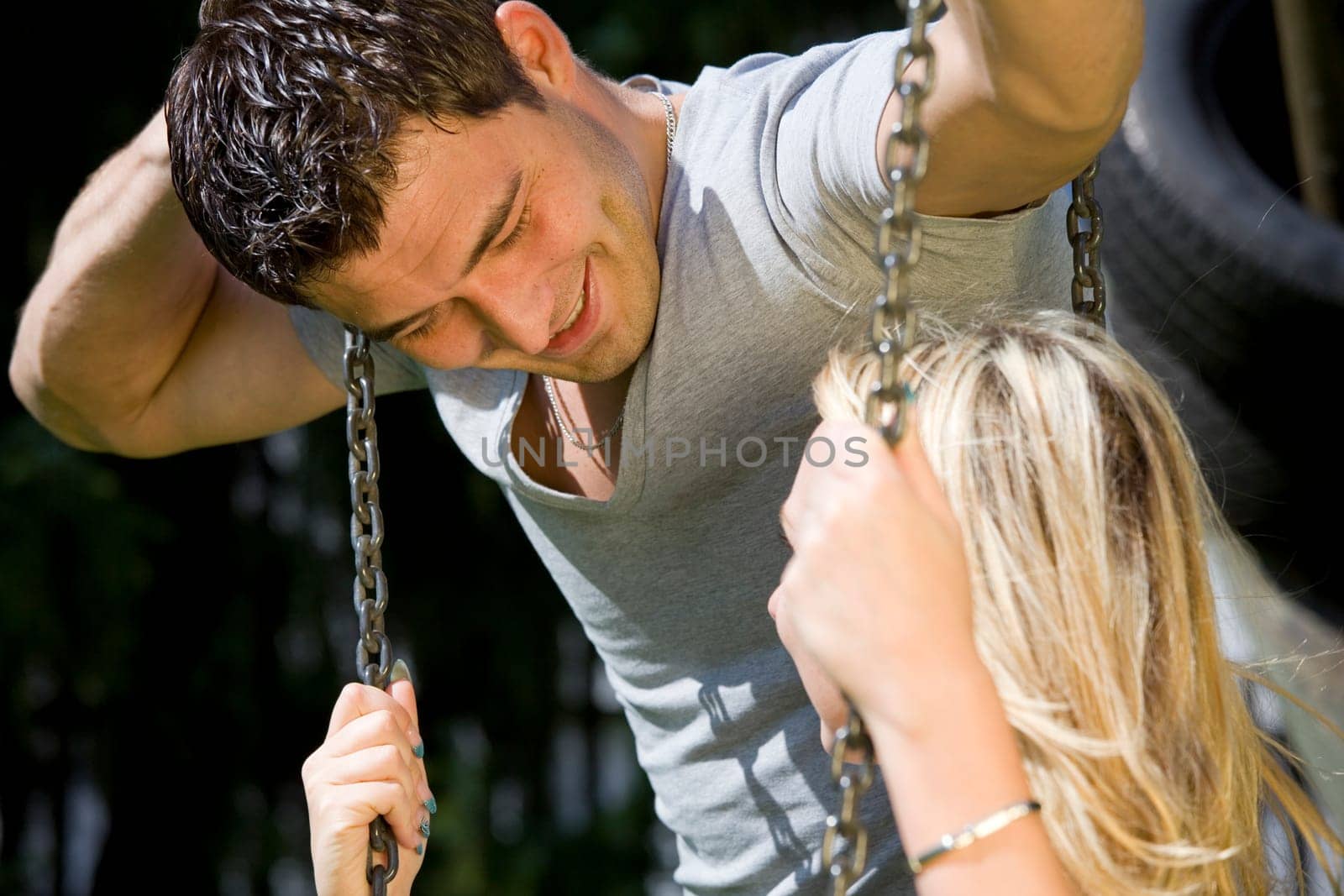 happy young couple talking on a swing in park