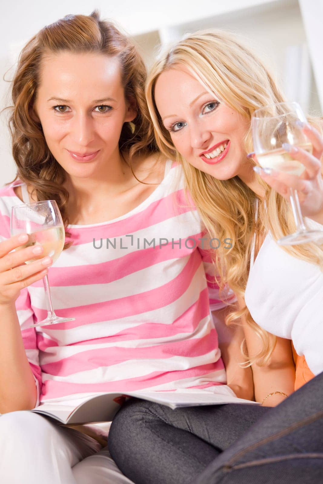 two women friends at home with magazine and glasses of wine