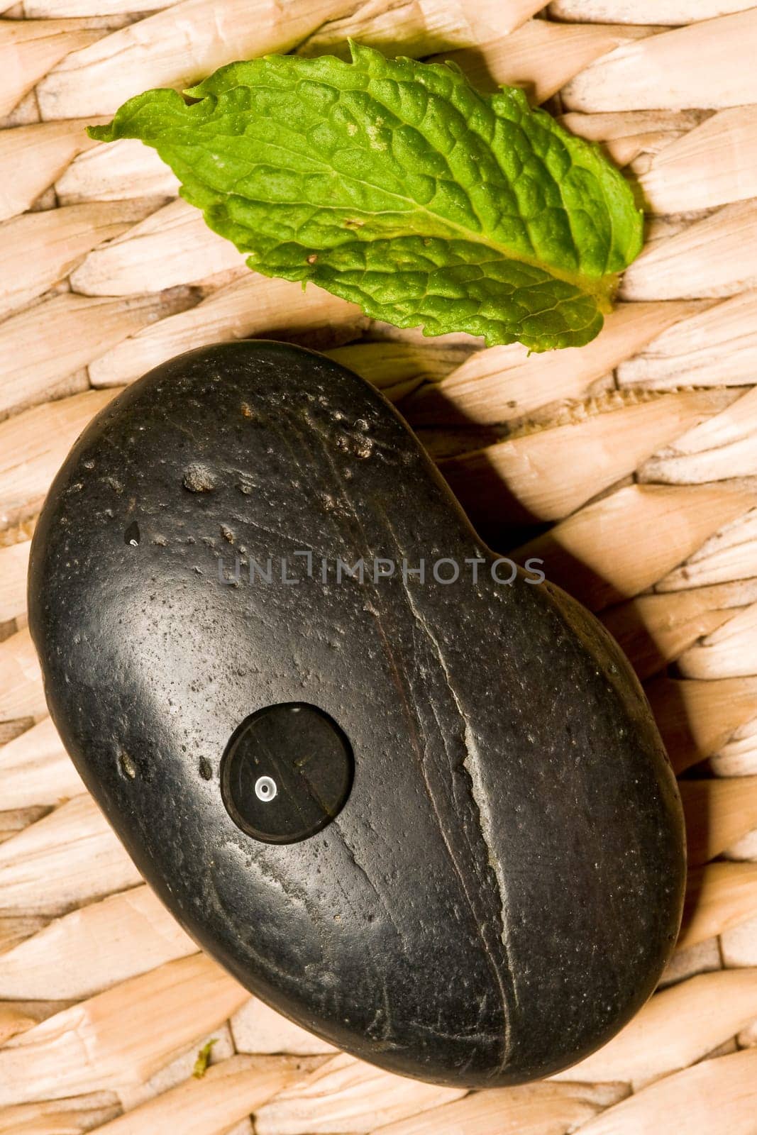 Black spa stone with a green leaf on wood mesh