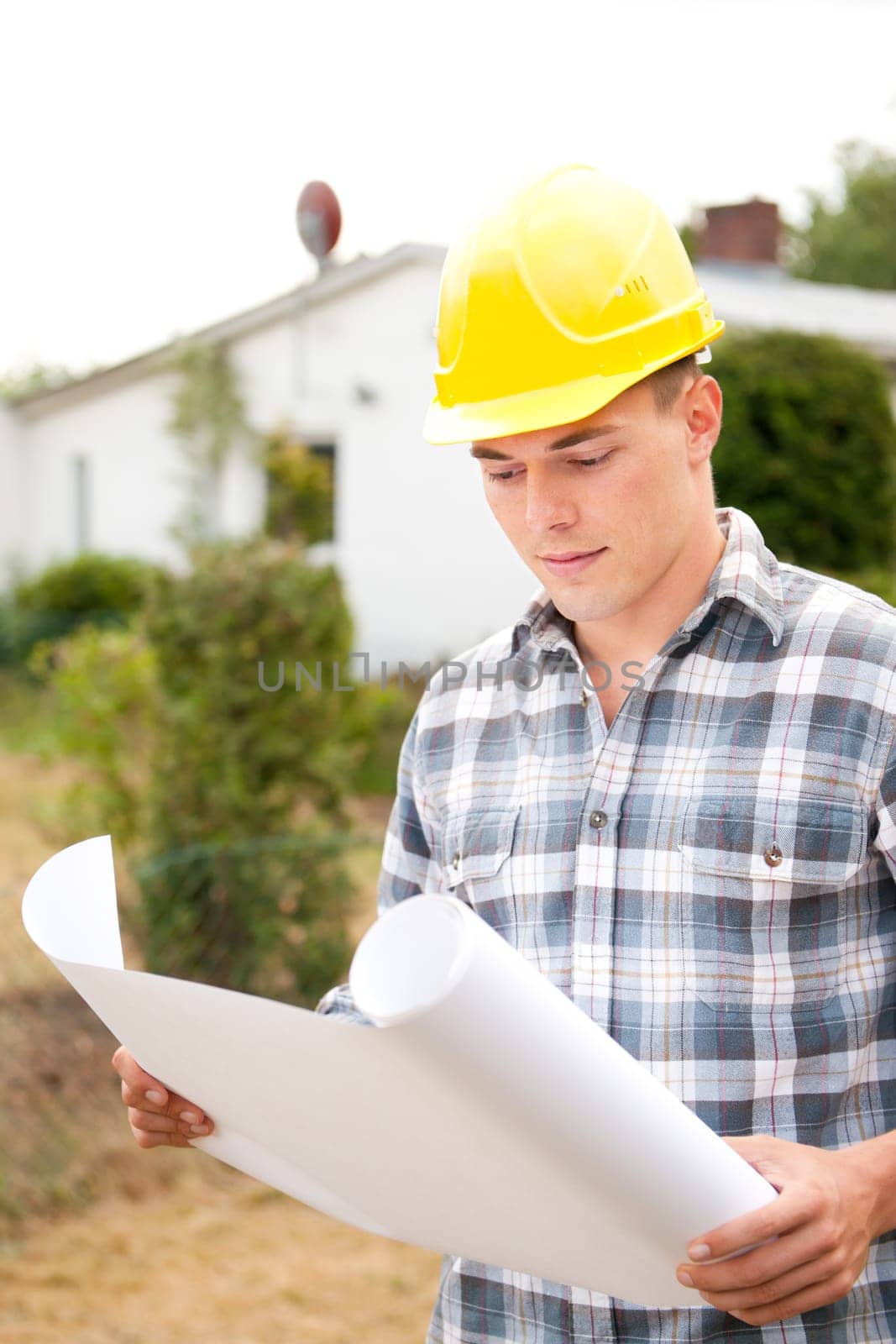 Young architect with a blueprint in front of a house