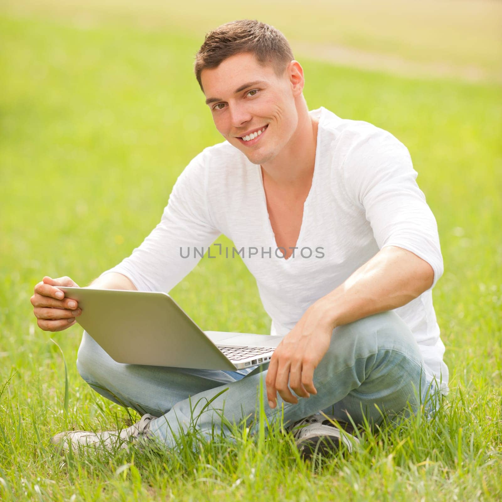 Young man with computer in a meadow