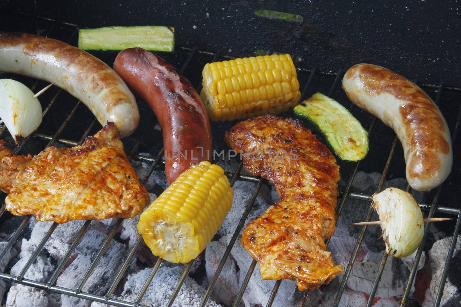 colorful grilled food on a charcoal grill with meat,sausages,corn,zucchini and onion