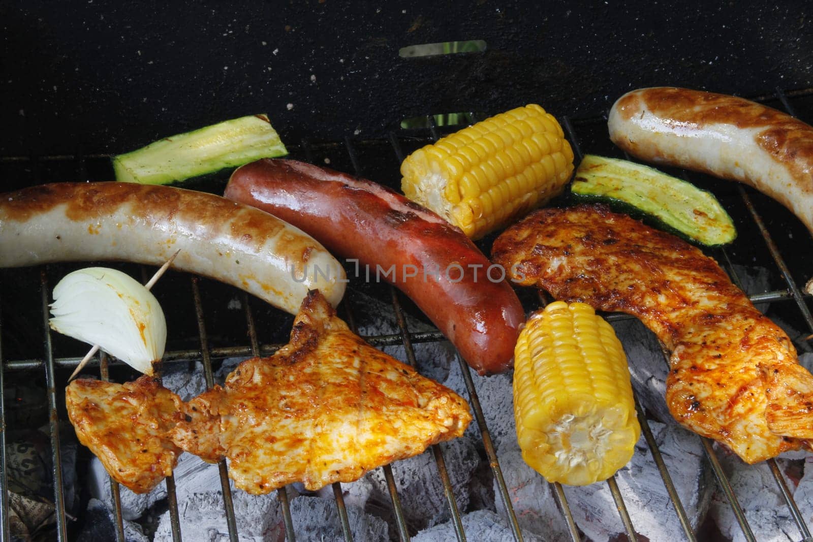 colorful grilled food on a charcoal grill with meat,sausages,corn,zucchini and onion