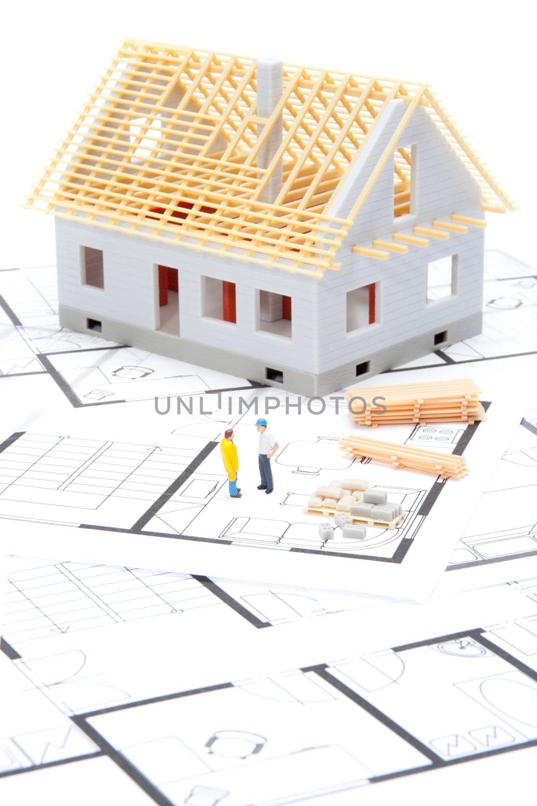 Building the house concept - model of the house with building material, builder figures and blueprints