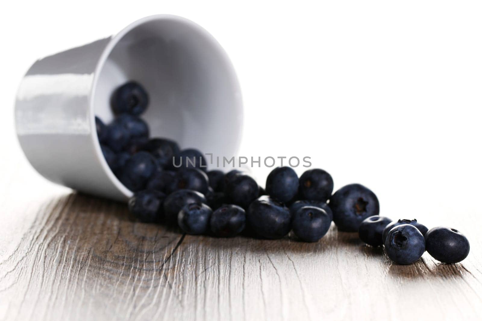 Blueberries rolling out of upside-down cup with backlight