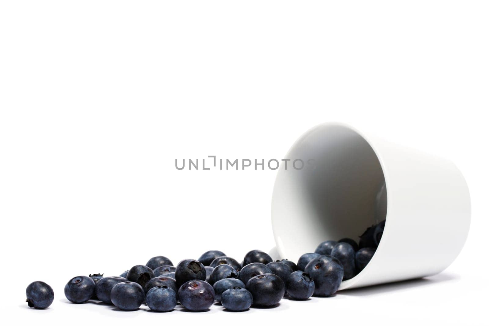 Blueberries rolling from overturned cup on white background