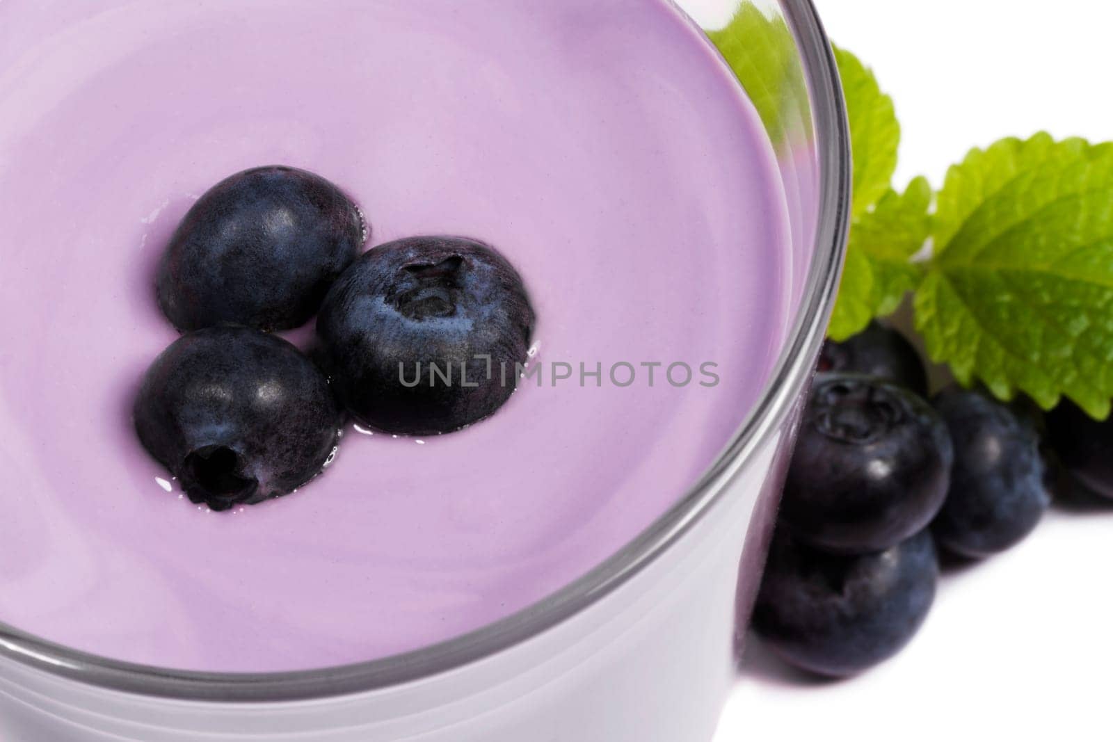 Blueberries on milkshake next to blueberries on white background