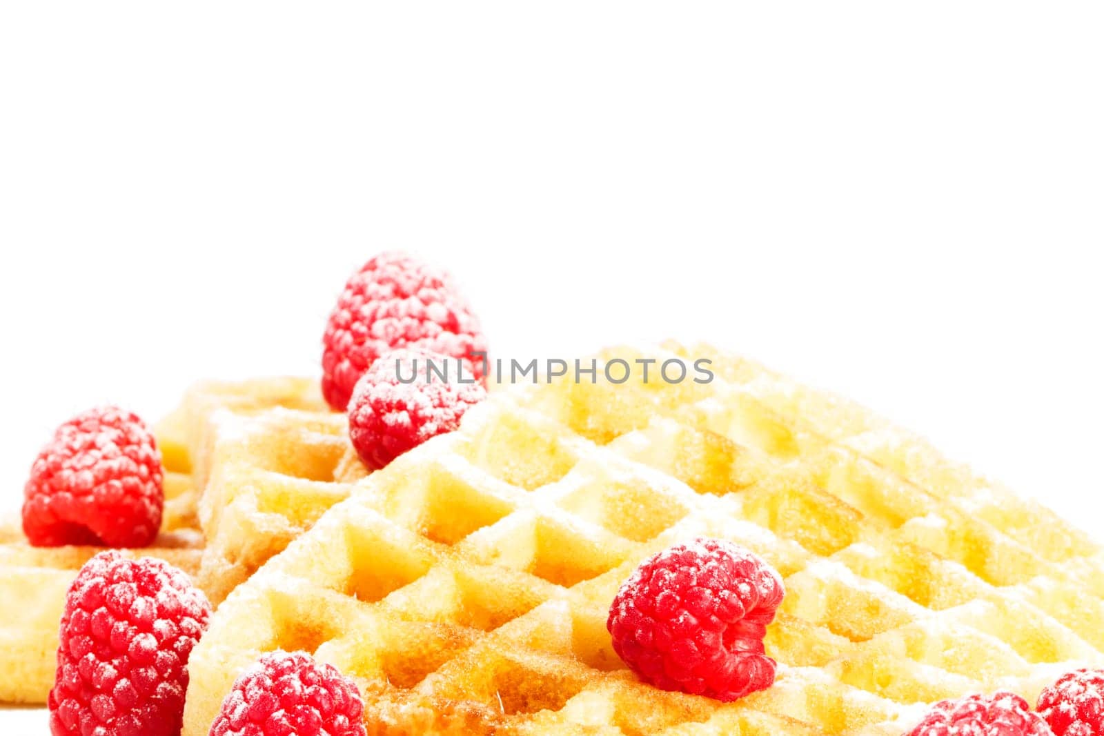 Sugared raspberries on waffles with syrup on white background