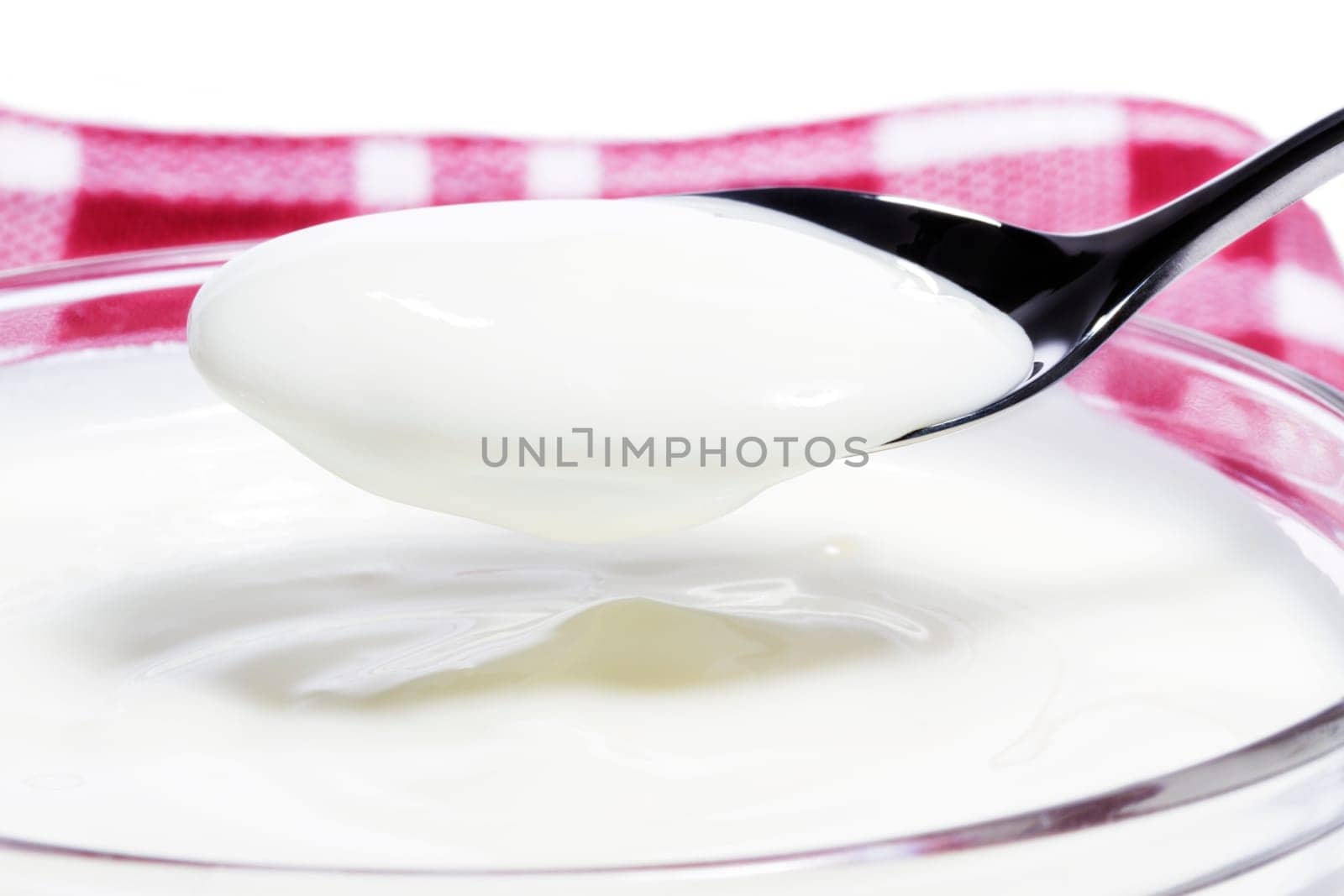 Yogurt on a spoon over a bowl on a cloth on a white background