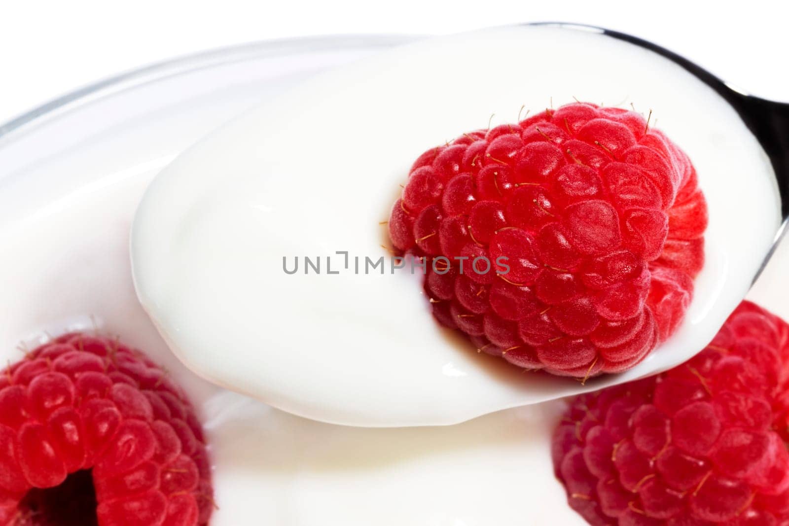 Raspberry on a spoon with yogurt from above on white background