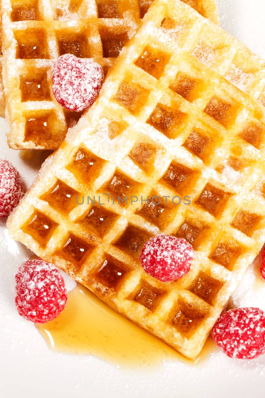 Sugared raspberries on waffles with syrup on white background