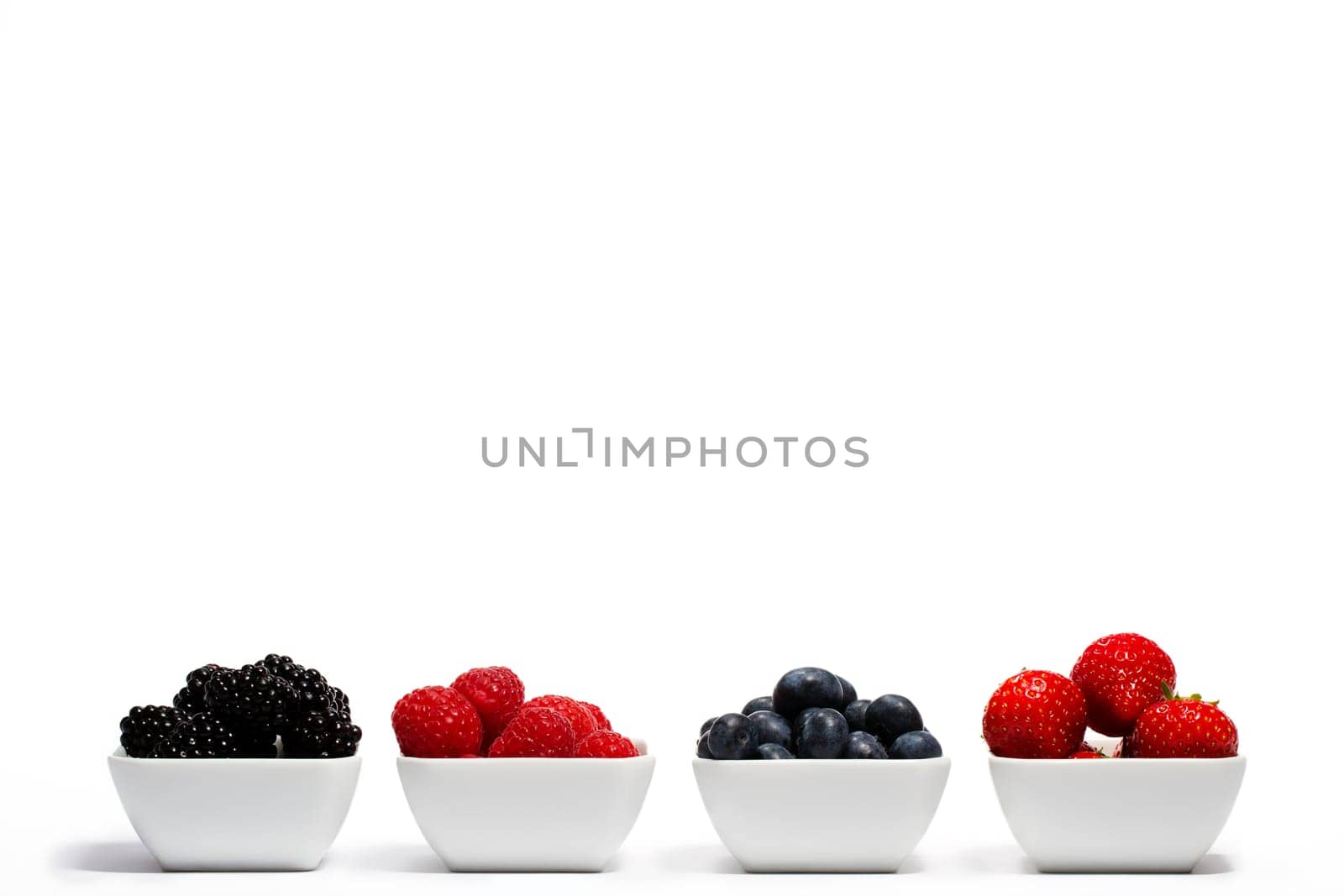 Wild berries in a row of bowls on white background