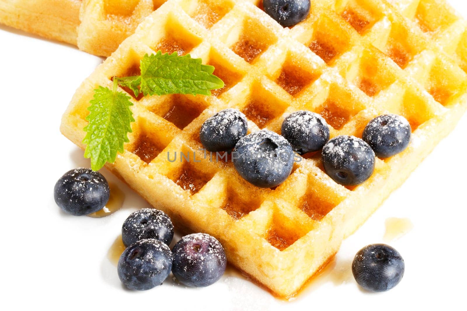 Waffles with sugared blueberries,lemon balm and syrup on white background