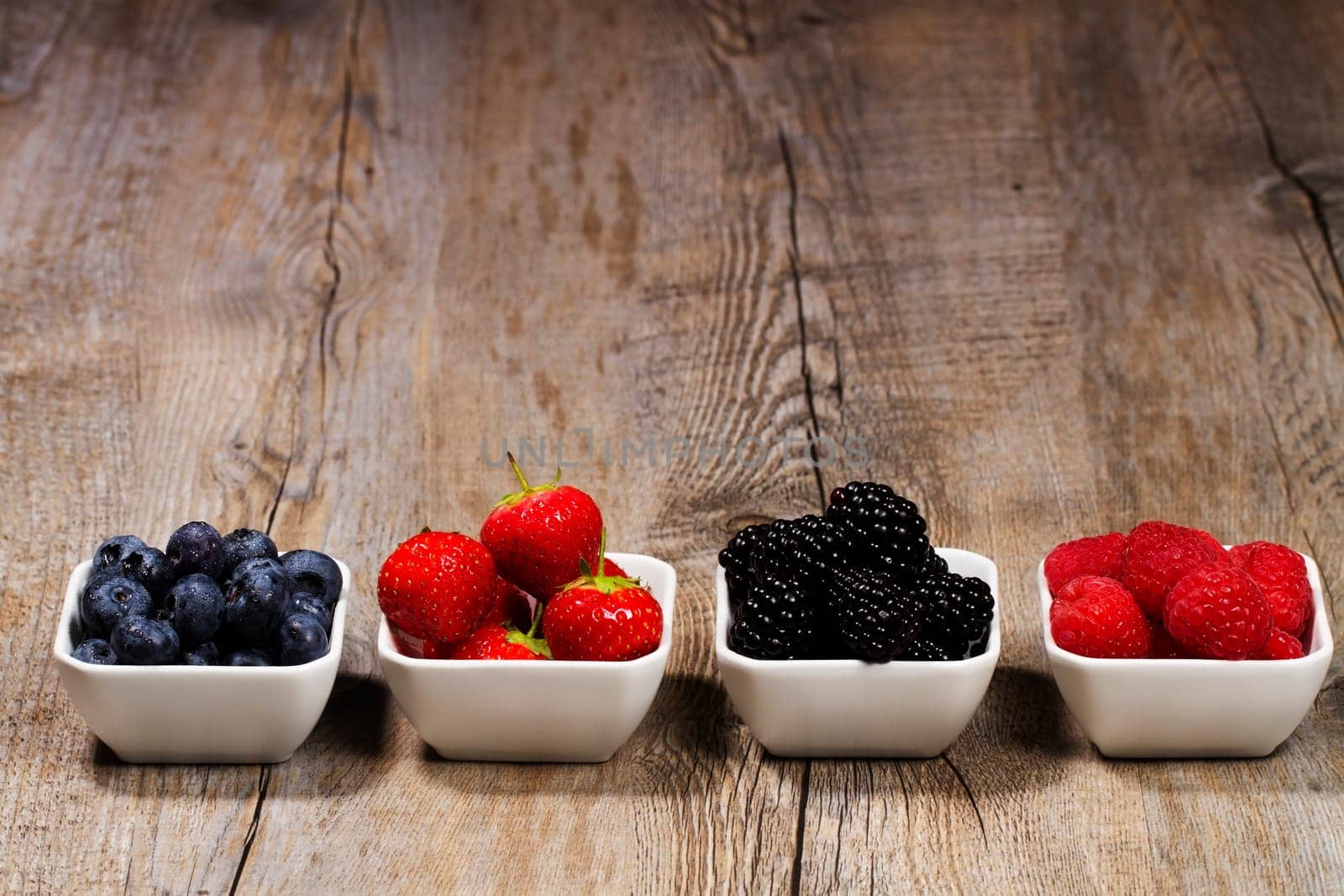 Set of bowls with wild berries on wooden background
