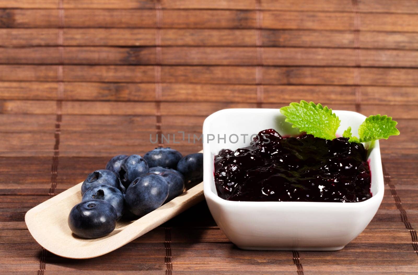 Blueberries jam next to blueberries on a shovel on wooden background