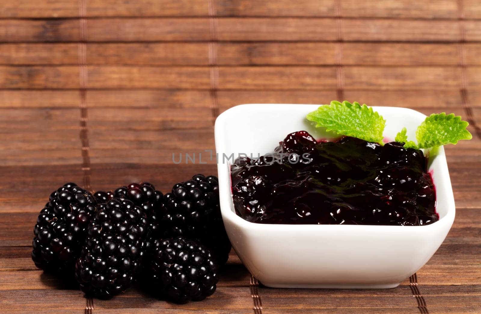 Blackberries jam next to blackberries on wooden background