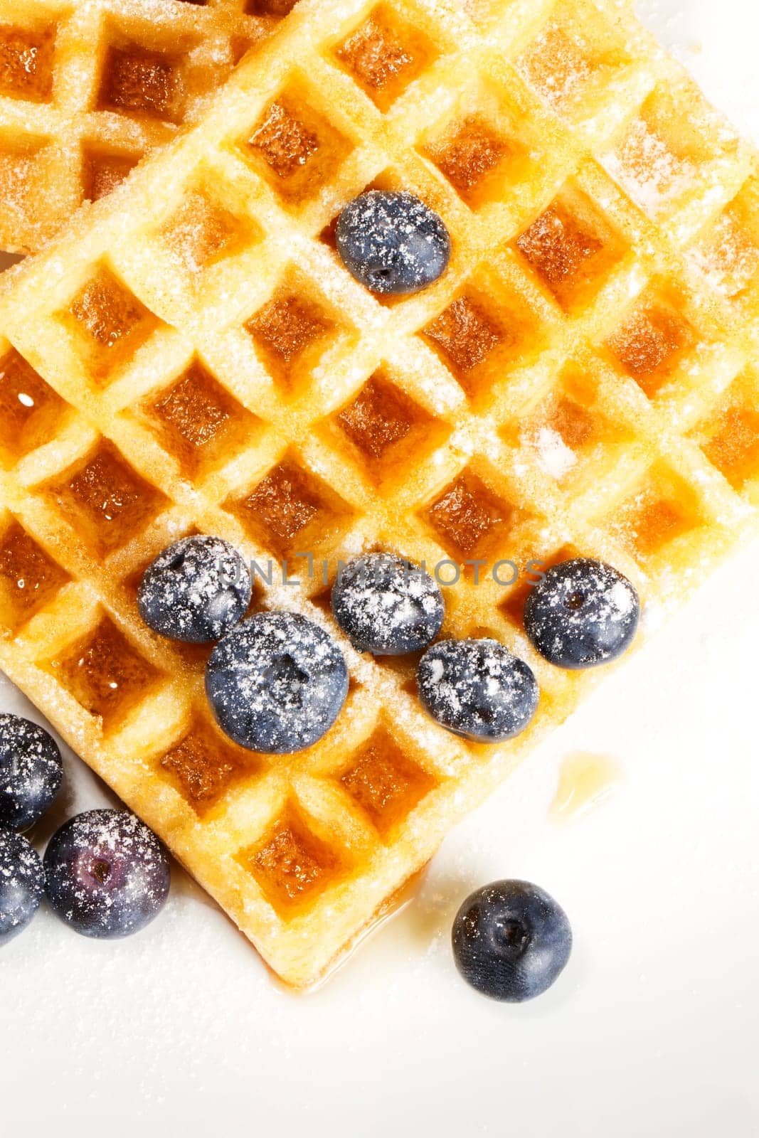 Waffles with sugared blueberries and syrup on white background