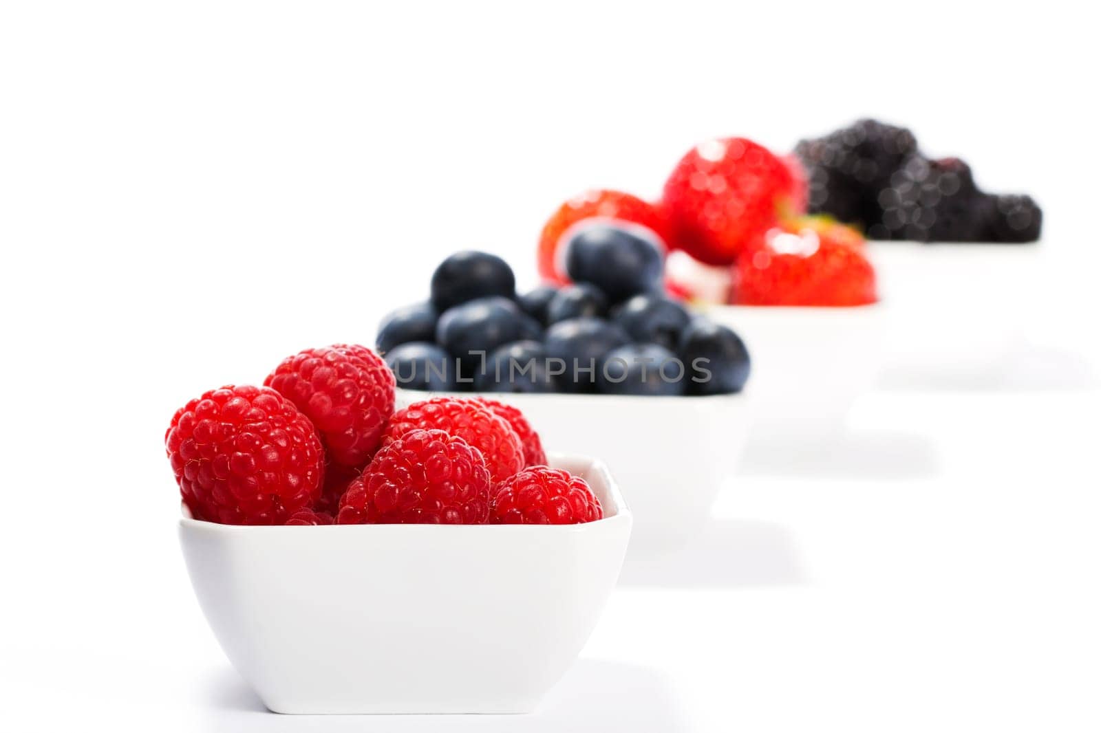 Raspberries in peel in front of other berries on white background
