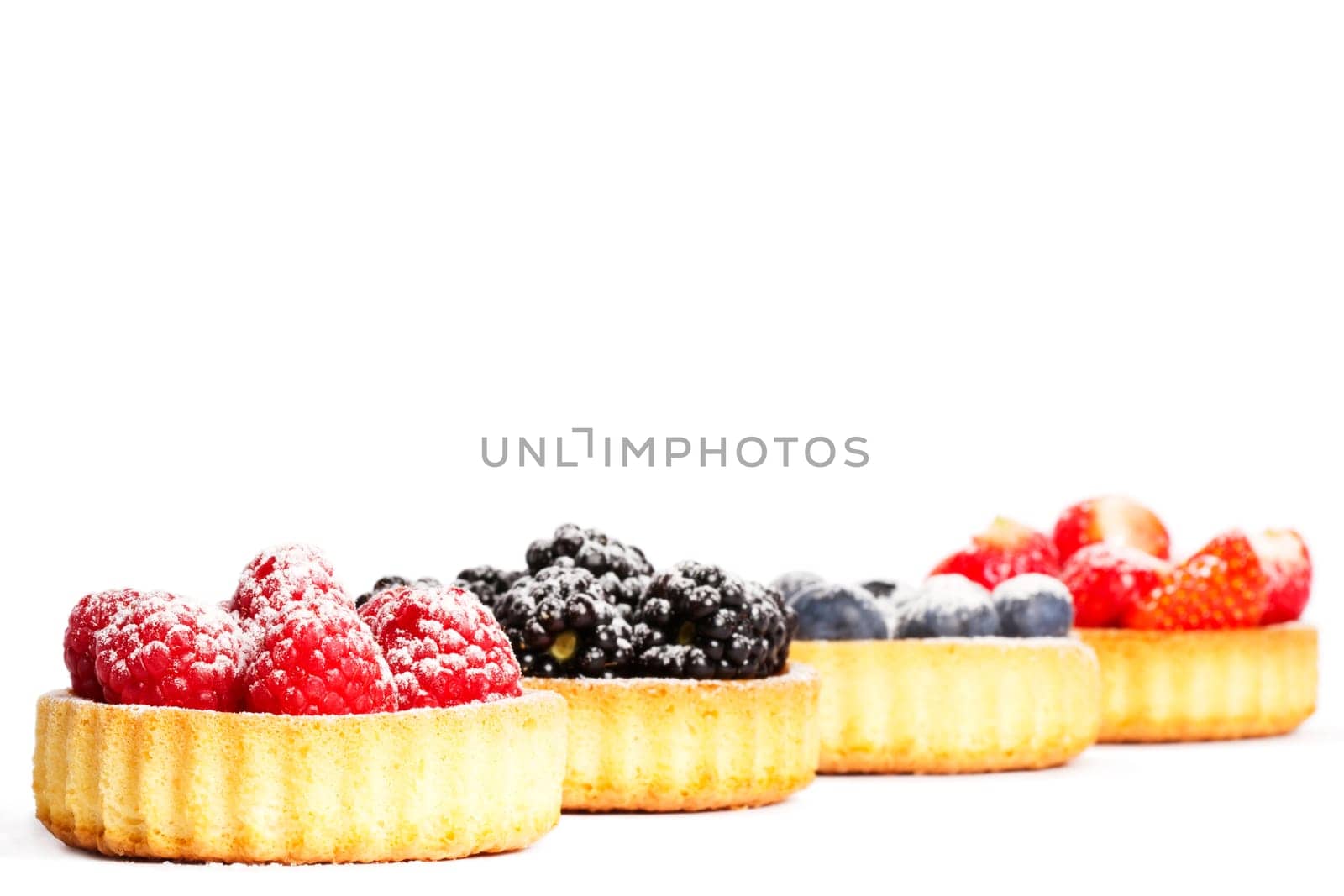 Sugared raspberries on tartlet cake in front of other berries on white background