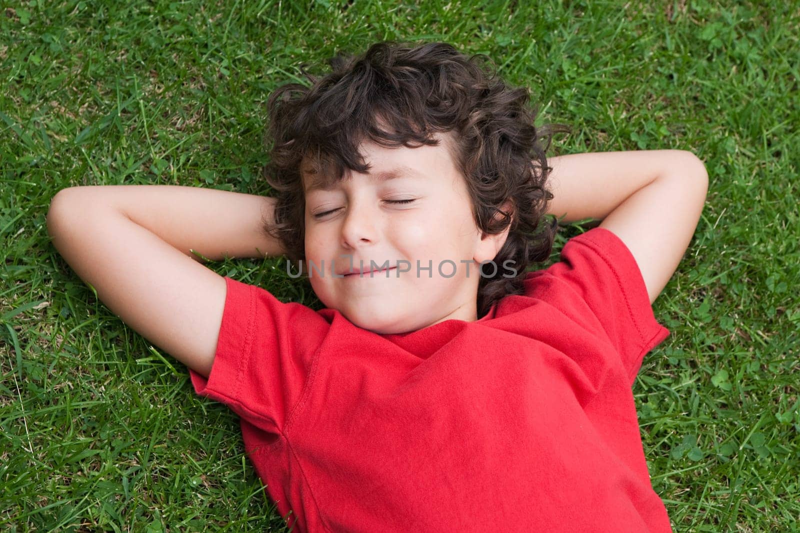 Happy child asleep on the grass with red shirt