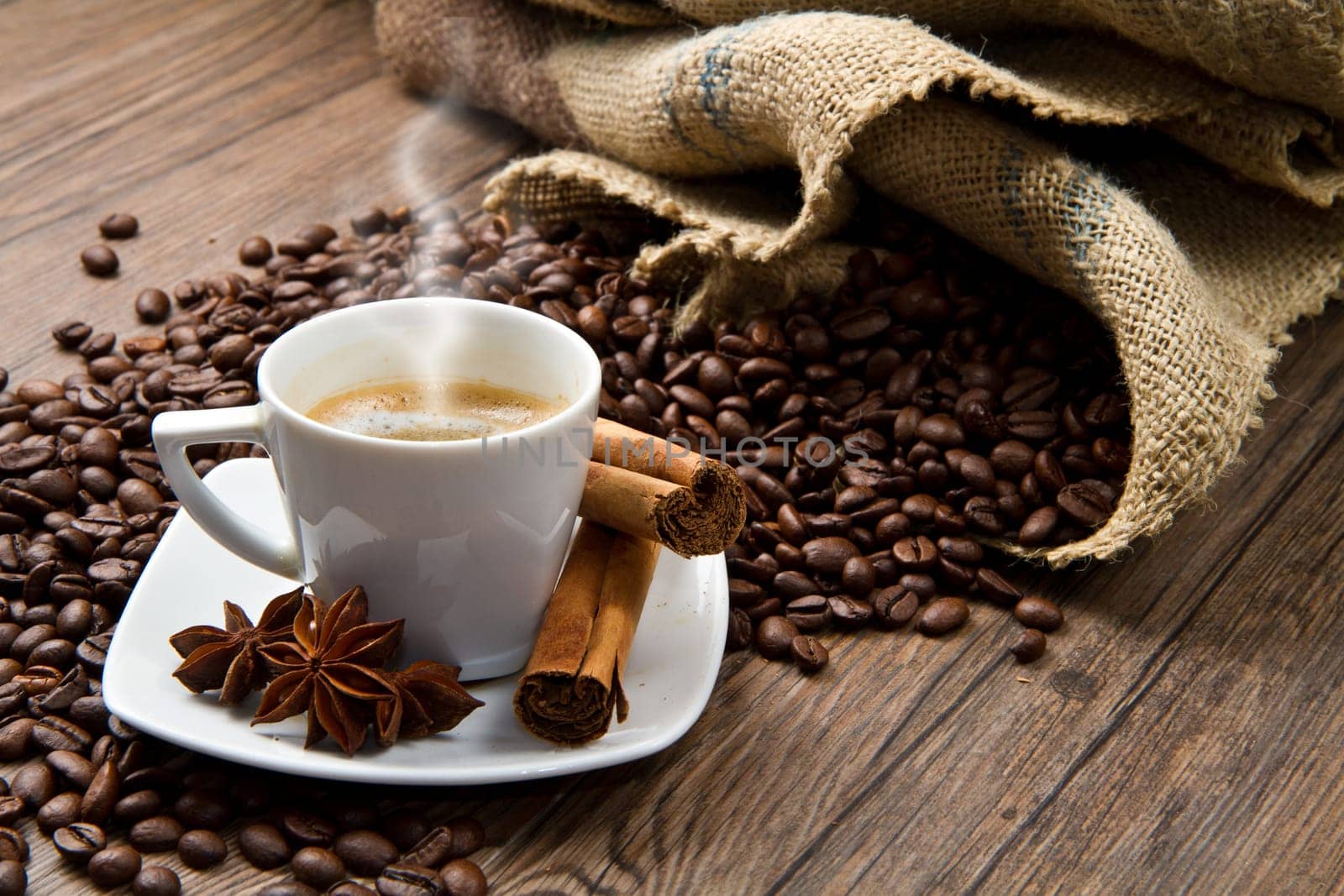 Coffee cup with burlap sack of roasted beans on rustic table