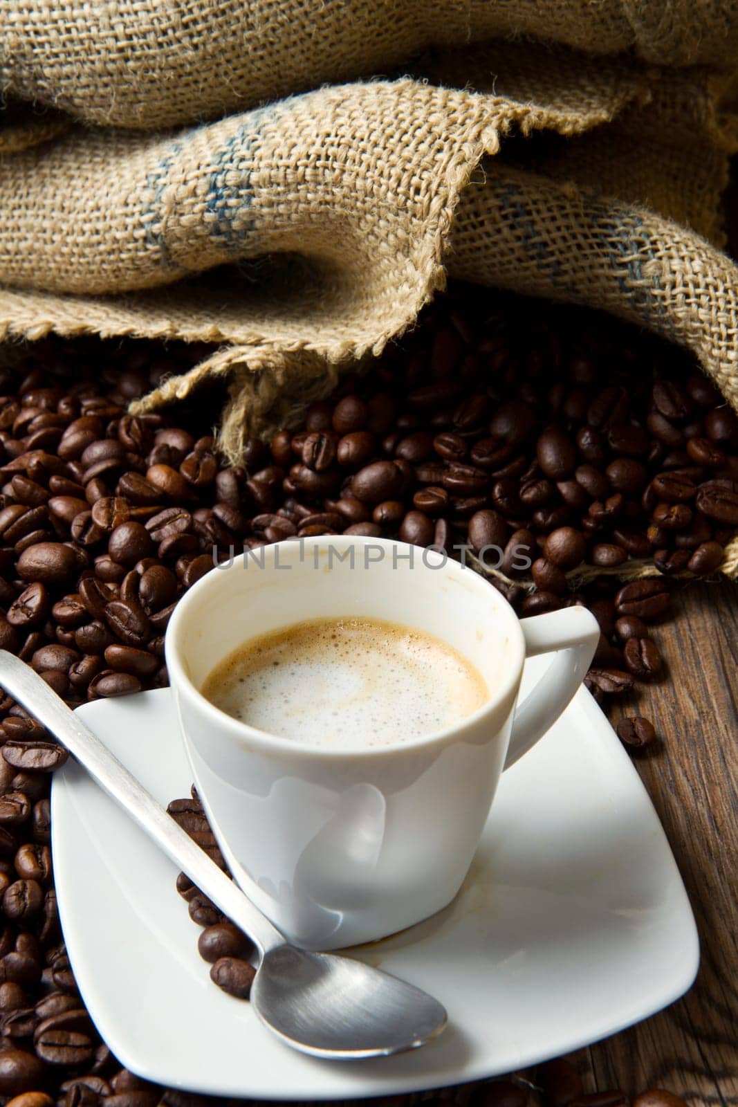 Coffee cup with burlap sack of roasted beans on rustic table
