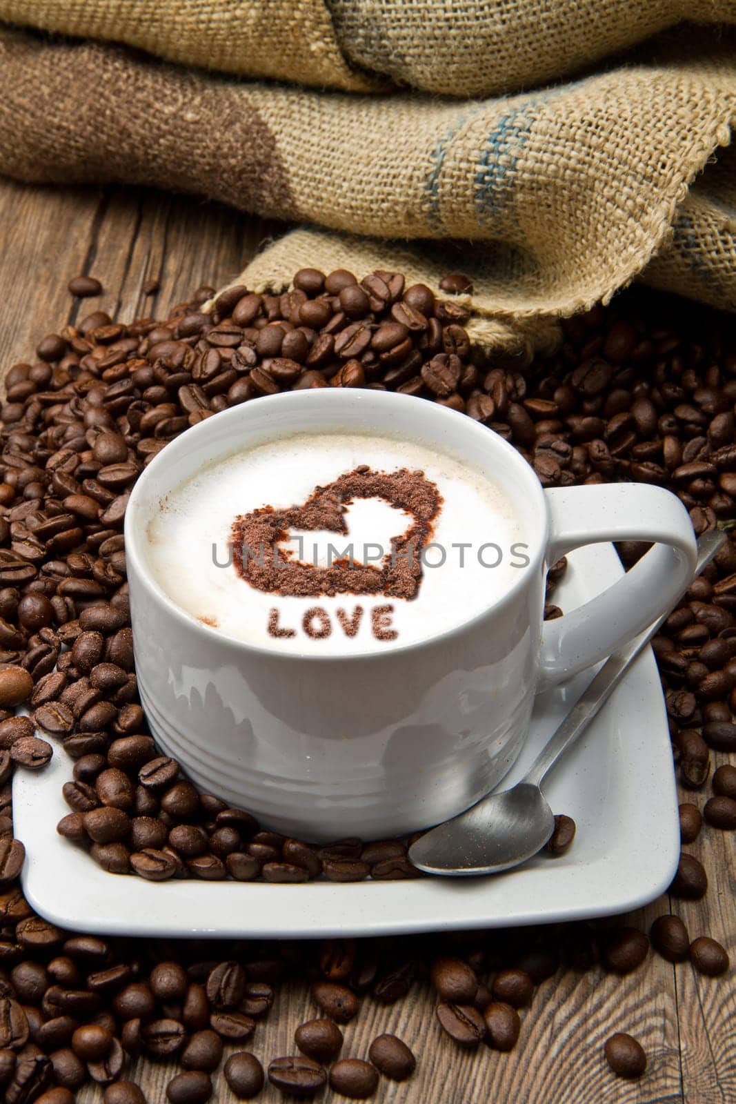 Coffee cup with burlap sack of roasted beans on rustic table