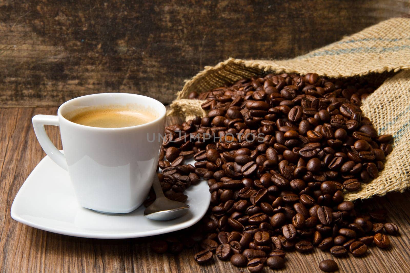 Coffee cup with burlap sack of roasted beans on rustic table