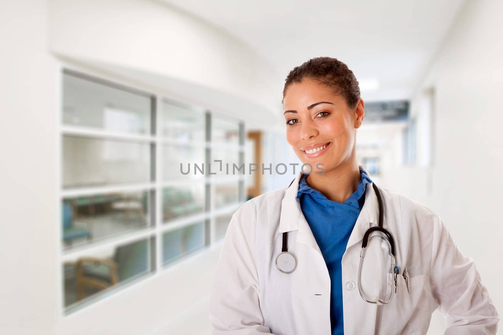 Beautiful attractive happy smiling female doctor physician nurse standing in hospital corridor hall way in front of patient consulting waiting area room.